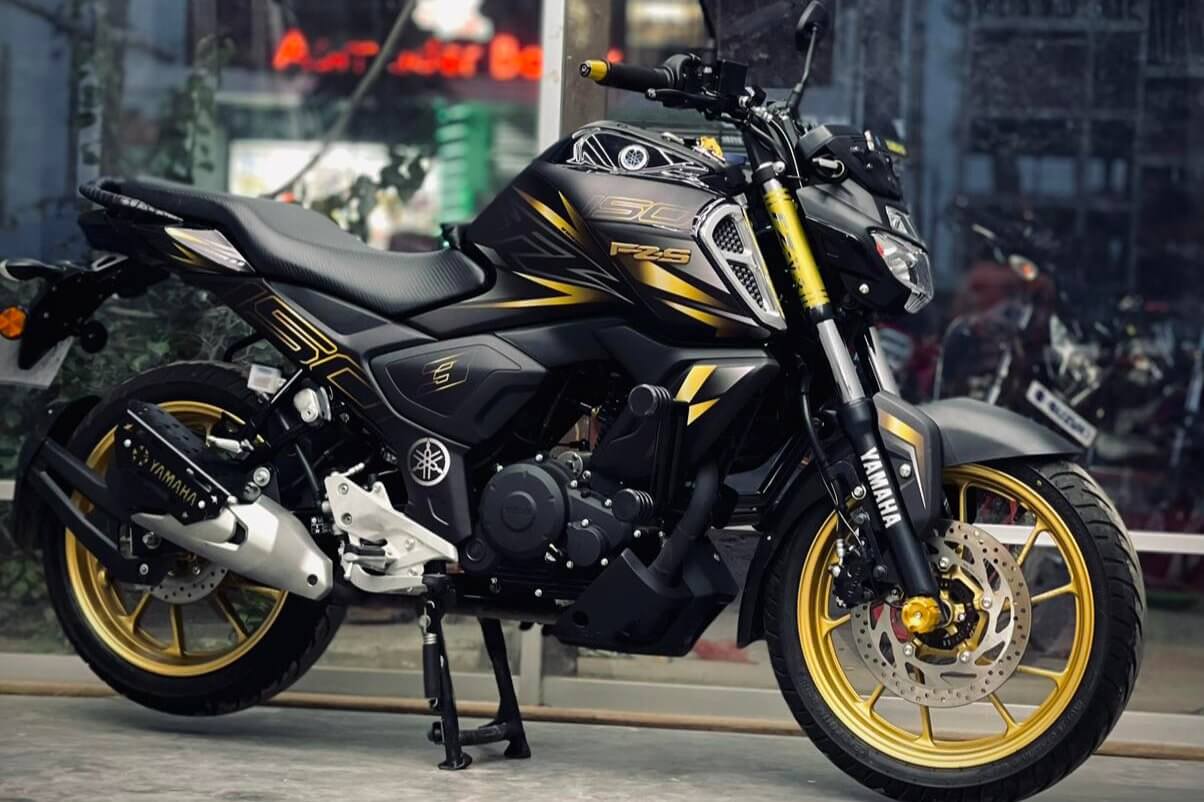 YAMAHA FZS V3/V4 motorcycle in black and gold displayed on a stand, shown in a store with glass windows in the background.