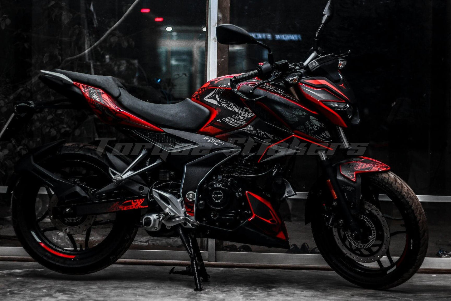 A black and red motorcycle with N160 Tribal decal kit, parked indoors with a reflective window behind.
